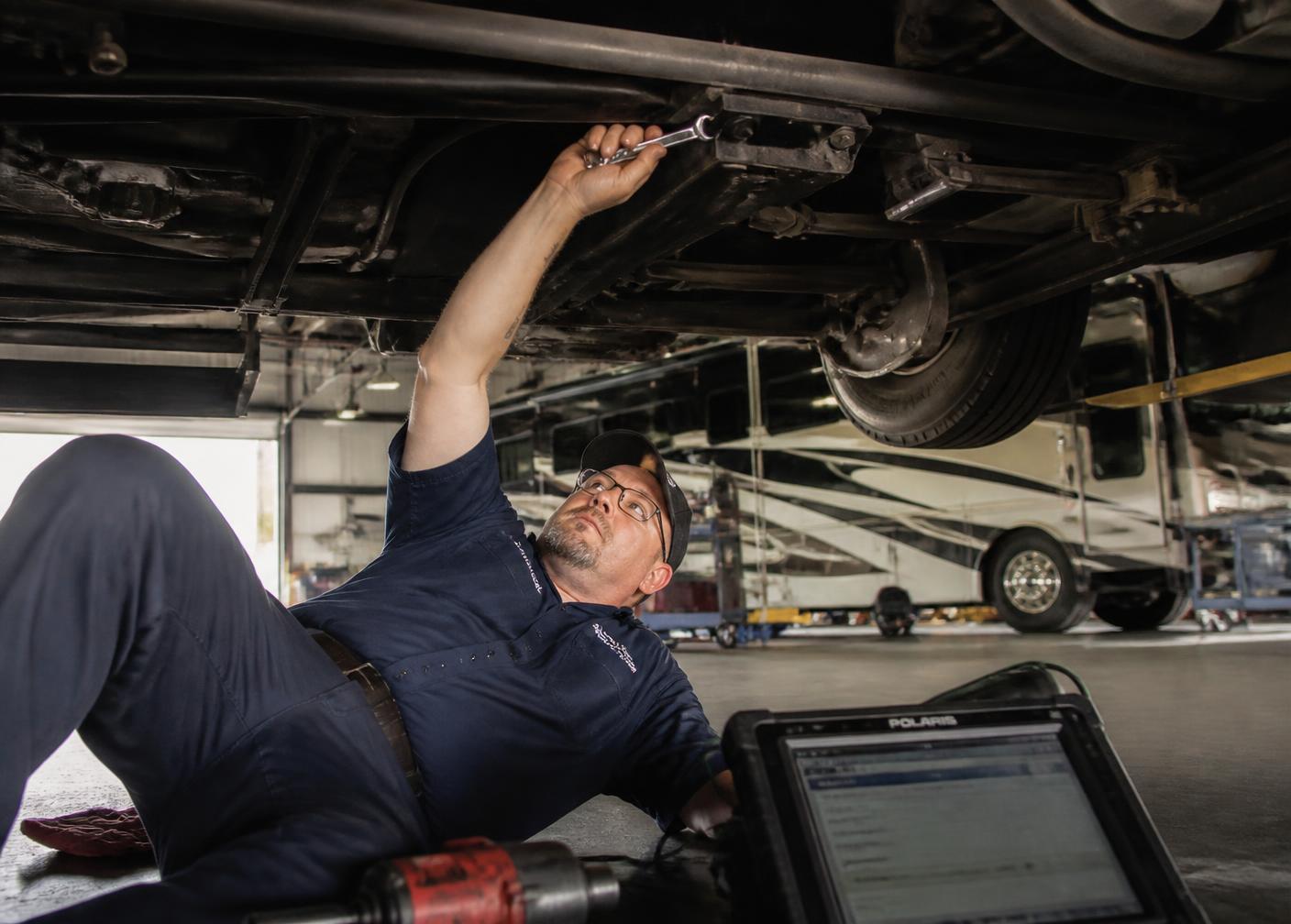 Technician under a motorhome chassis servicing suspension components